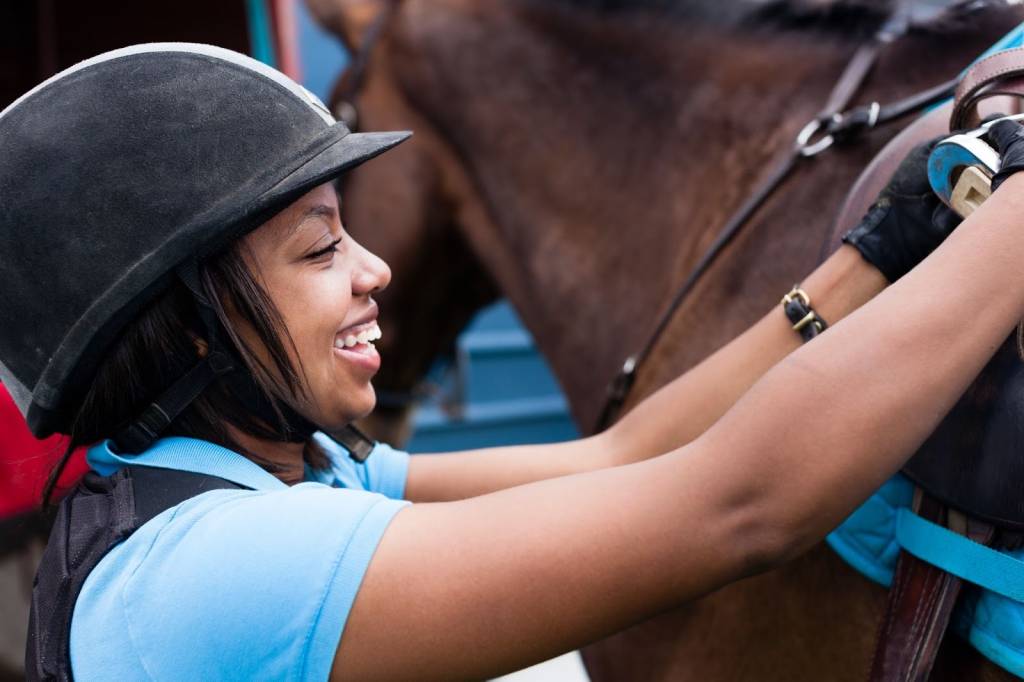 A girl is adjusting a saddle on a horse.