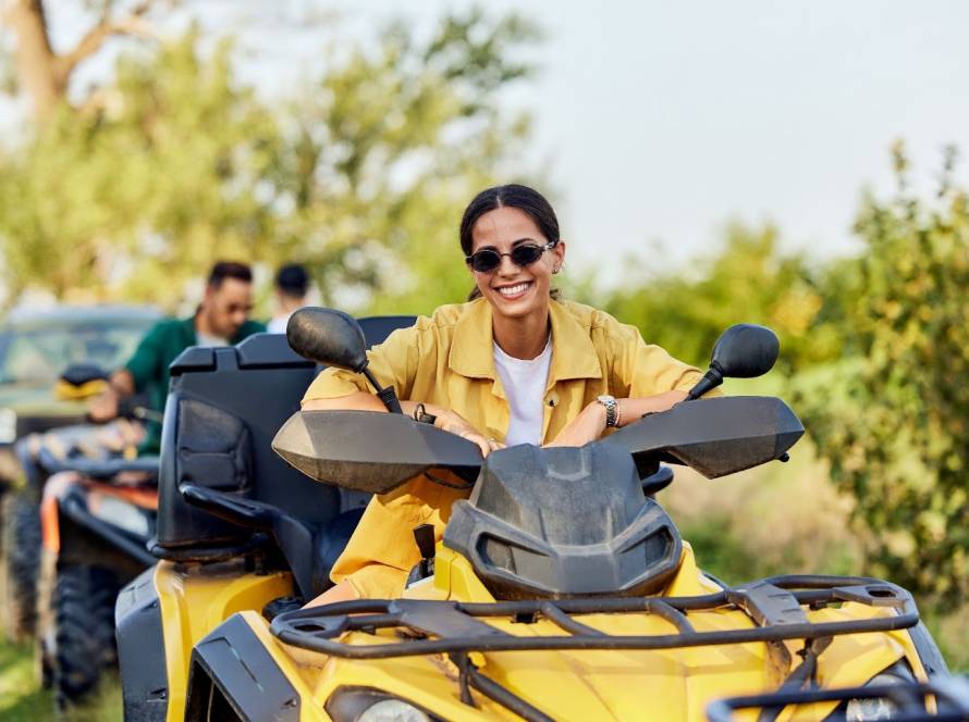 A woman in a yellow polo and shades prepares to drive a rental four-wheeler through a scenic nature trail.
