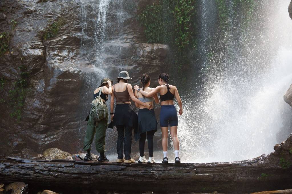 Four ladies enjoying the waterfall view from a log while on a nature excursion.