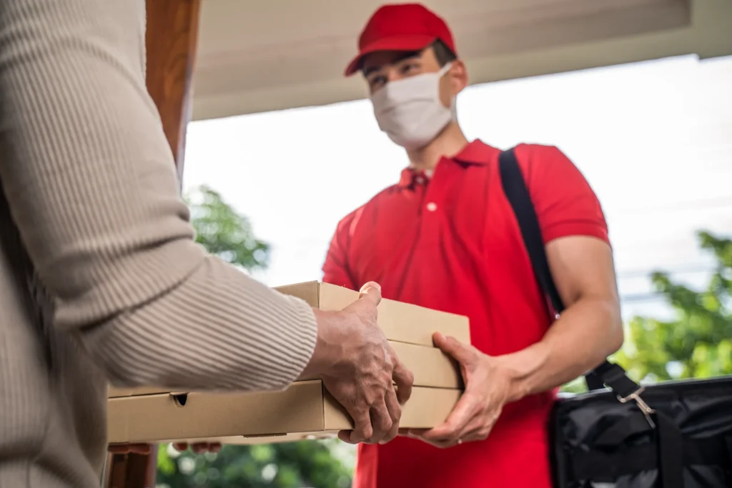 Pizza delivery driver handing pizza boxes to a customer at the door.